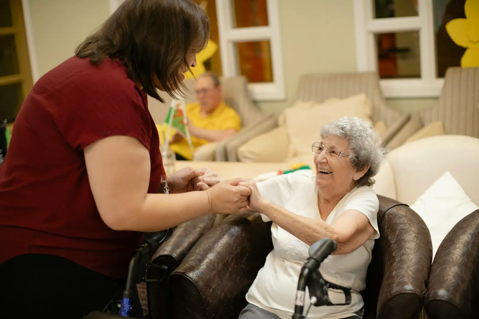 A carer holding hands with a smiling resident in a care home lounge